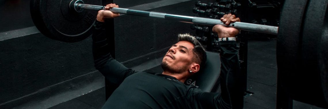 Man performing bench press with heavy barbell in a gym setting, focusing on strength training.